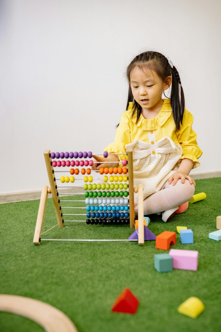 A little girl in a yellow shirt is sitting on the floor playing with a colorful abacus and toy blocks.